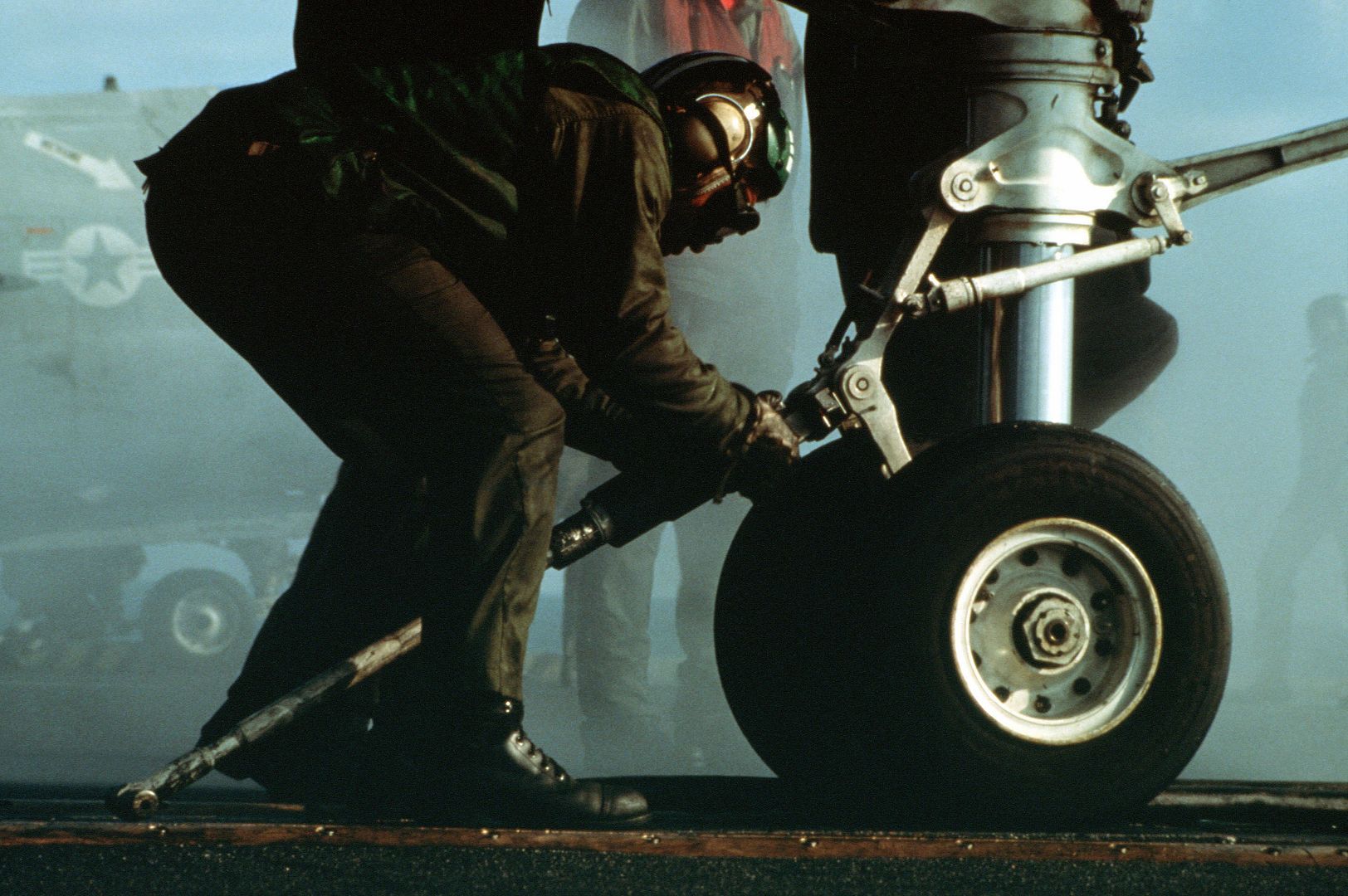 A flight deck crewman attaches the holdback bar on an F14 Tomcat
